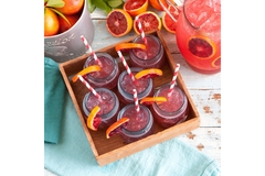 Glasses of blood orange juice with ice and striped straws, served with fresh citrus slices in a wooden tray